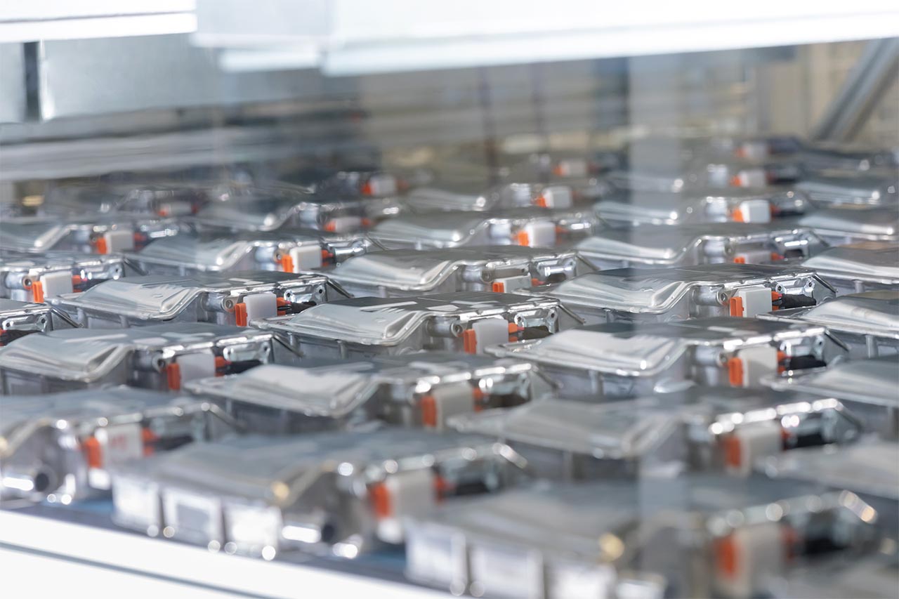 Dense array of rectangular HV battery housings with orange connectors on assembly trays, illustrating Webasto battery systems production and inspection.