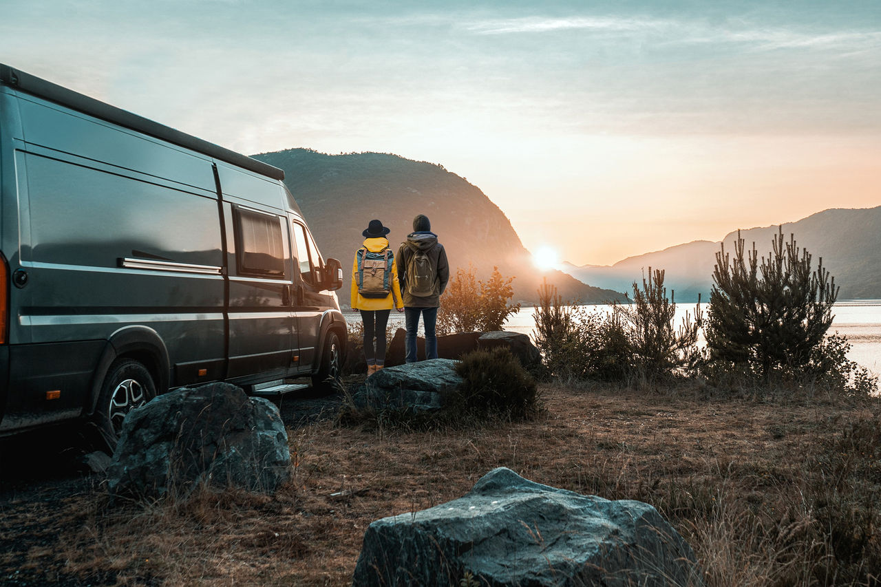 Camper van at lakeside sunrise with two travelers, illustrating mobile comfort and integration for Webasto roof systems, heaters and battery solutions for RVs.