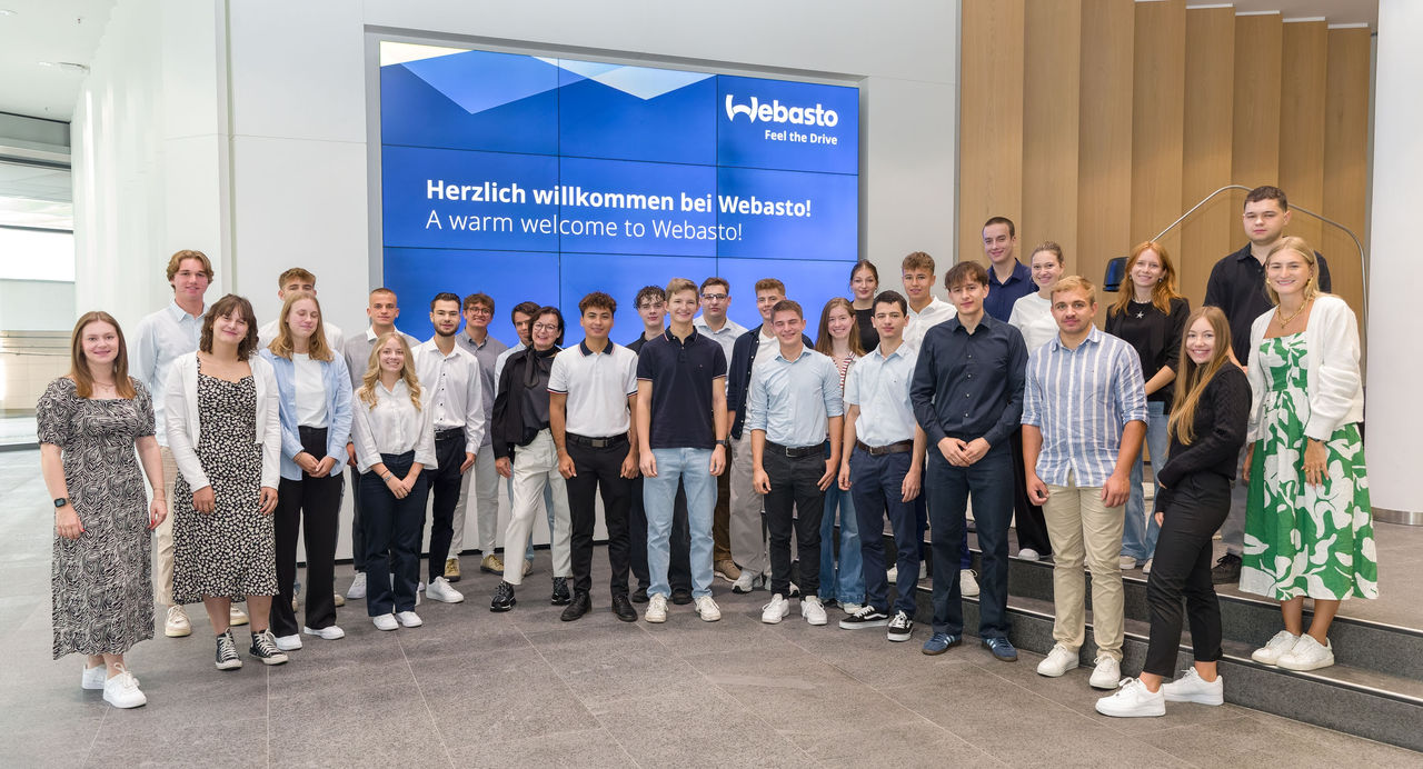 New hires at Webasto HQ reception with bilingual welcome signage for careers pages, highlighting onboarding and Webasto as a global systems partner.