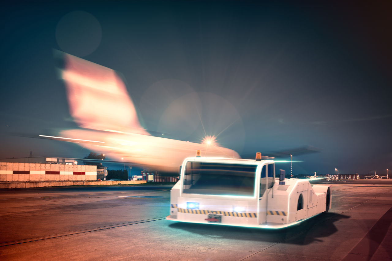 Night airport scene with electrified tow tractor and aircraft, for vehicle solutions highlighting Webasto as system partner for ground-support electrification.