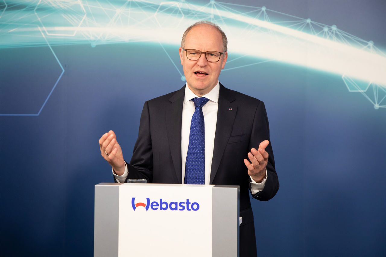 Spokesperson at Webasto podium with digital network backdrop, newsroom asset for press releases and announcements highlighting Webasto's system partner role.