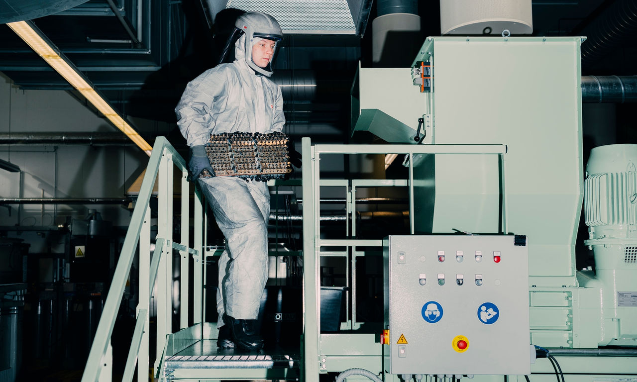 Technician in protective gear handling an EV battery module on a production platform, illustrating Webasto battery-systems manufacturing and safety protocols.