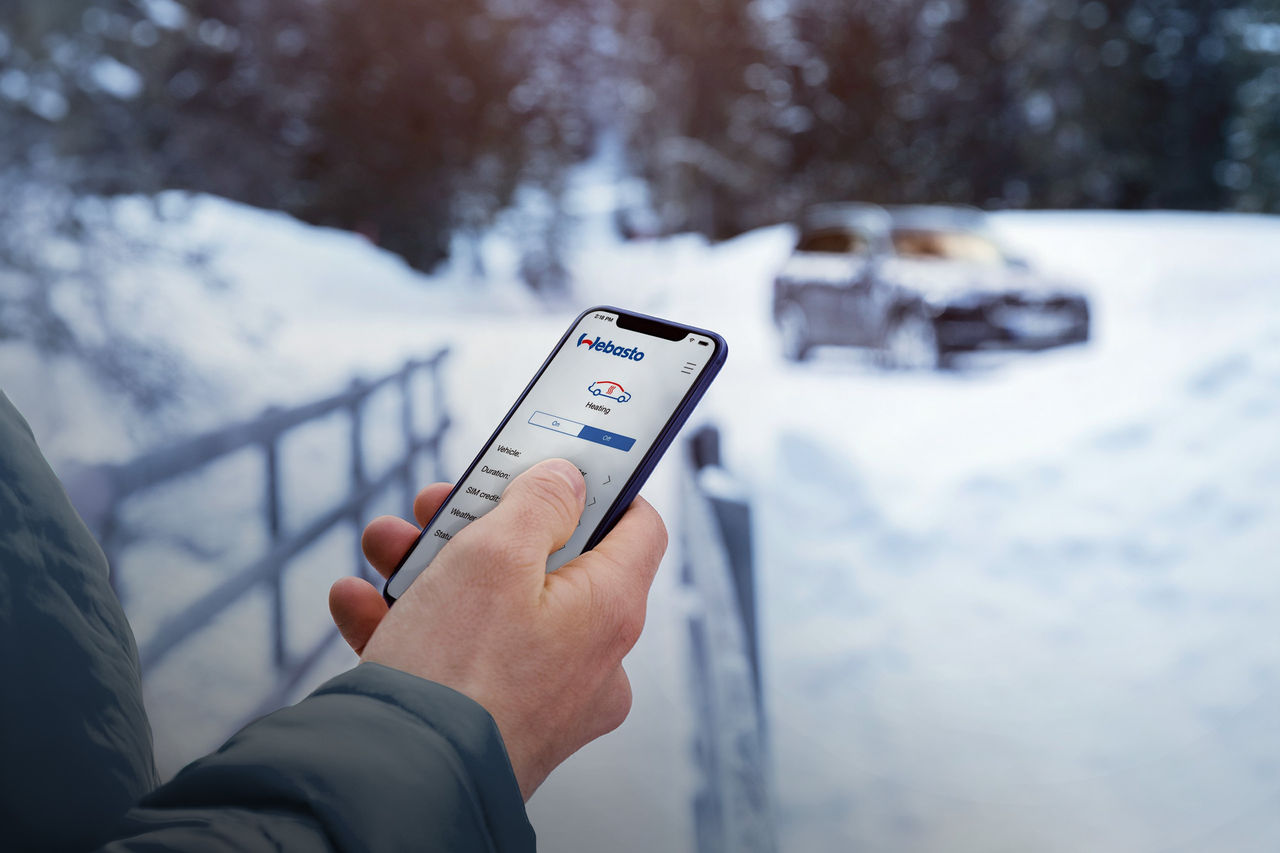 Handheld smartphone displaying Webasto ThermoConnect app controlling a parking heater for remote pre-conditioning, part of Webasto thermal management.